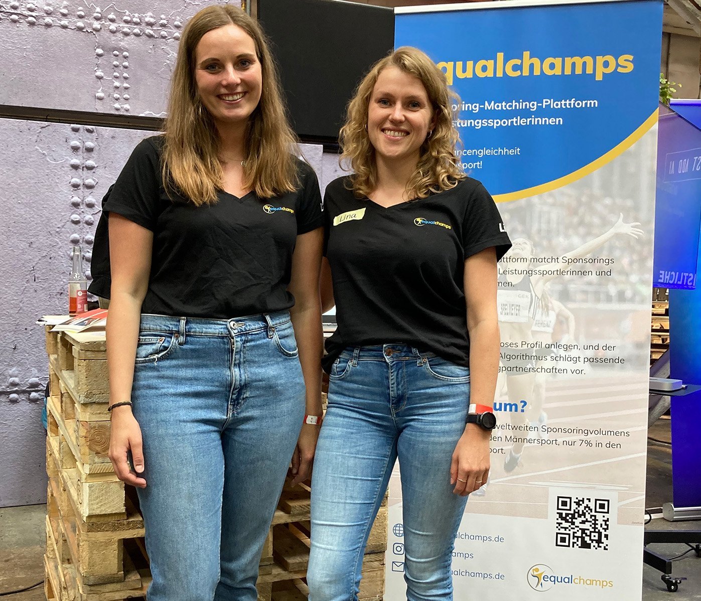 Die beiden Gründerinnen stehen vor einem Plakat von equalchamps