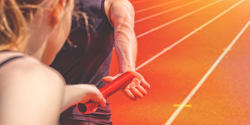 Eine Sportlerin übergibt die Staffel im Staffellauf. 
